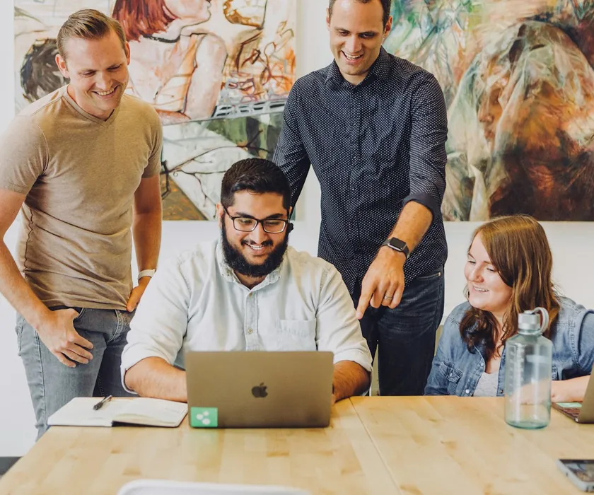 Four coworkers gathered around a laptop, smiling