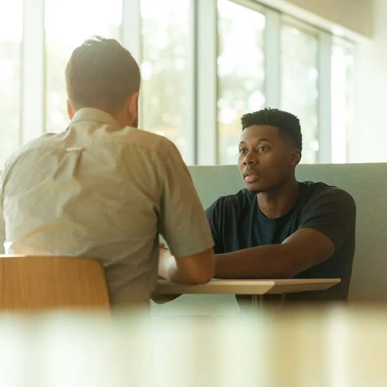 Two colleagues talking across a table in a sunlit office